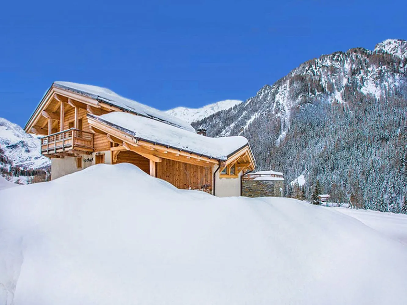 Chalet Cairn im Tiefschnee unter blauem Himmel, dahinter verschneite Gipfel