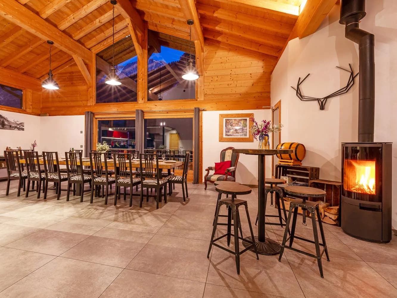 Das Loft im Chalet Cairn am Abend mit langer Tafel und brennendem Kaminofen