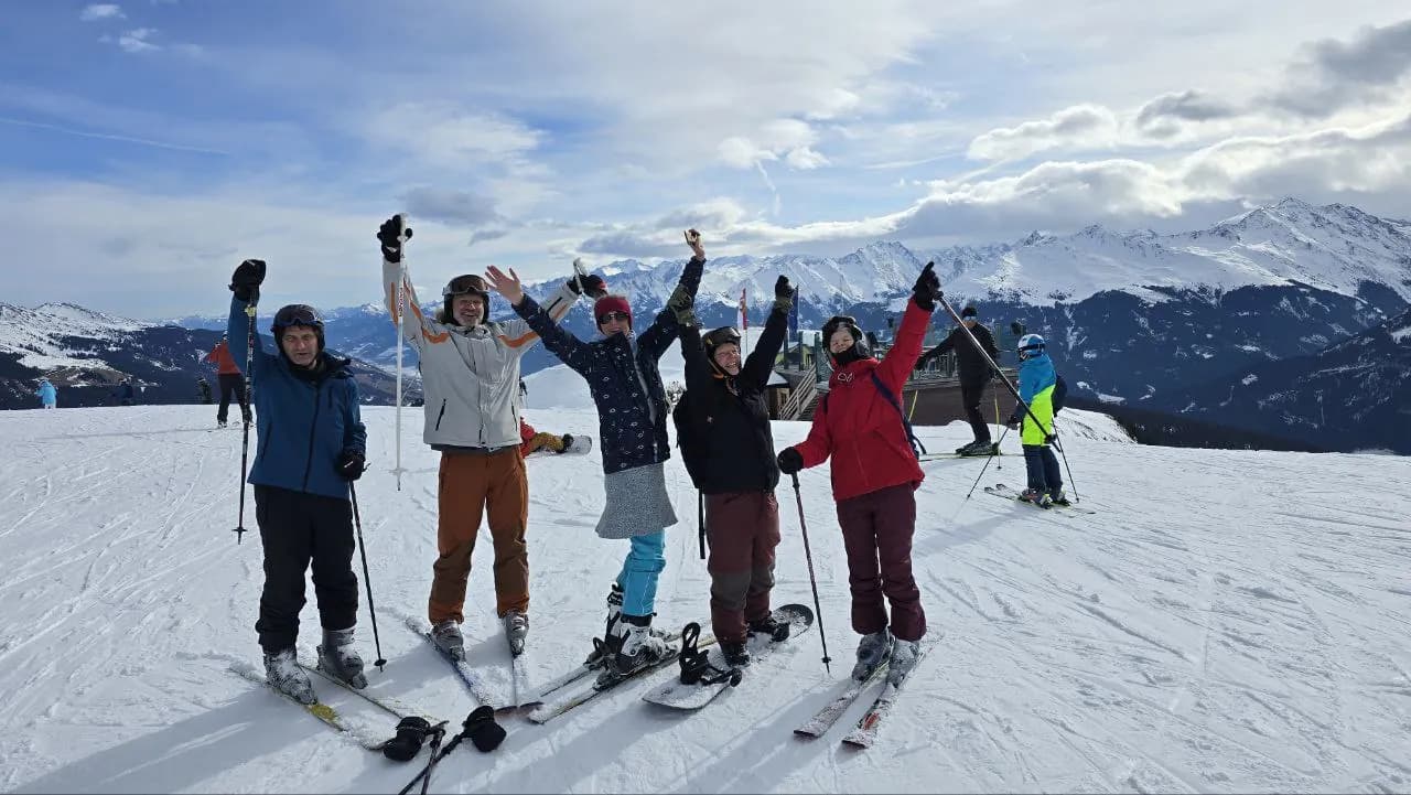Eine Gruppe auf Skiern jubelt mit erhobenen Armen auf einem Gipfel