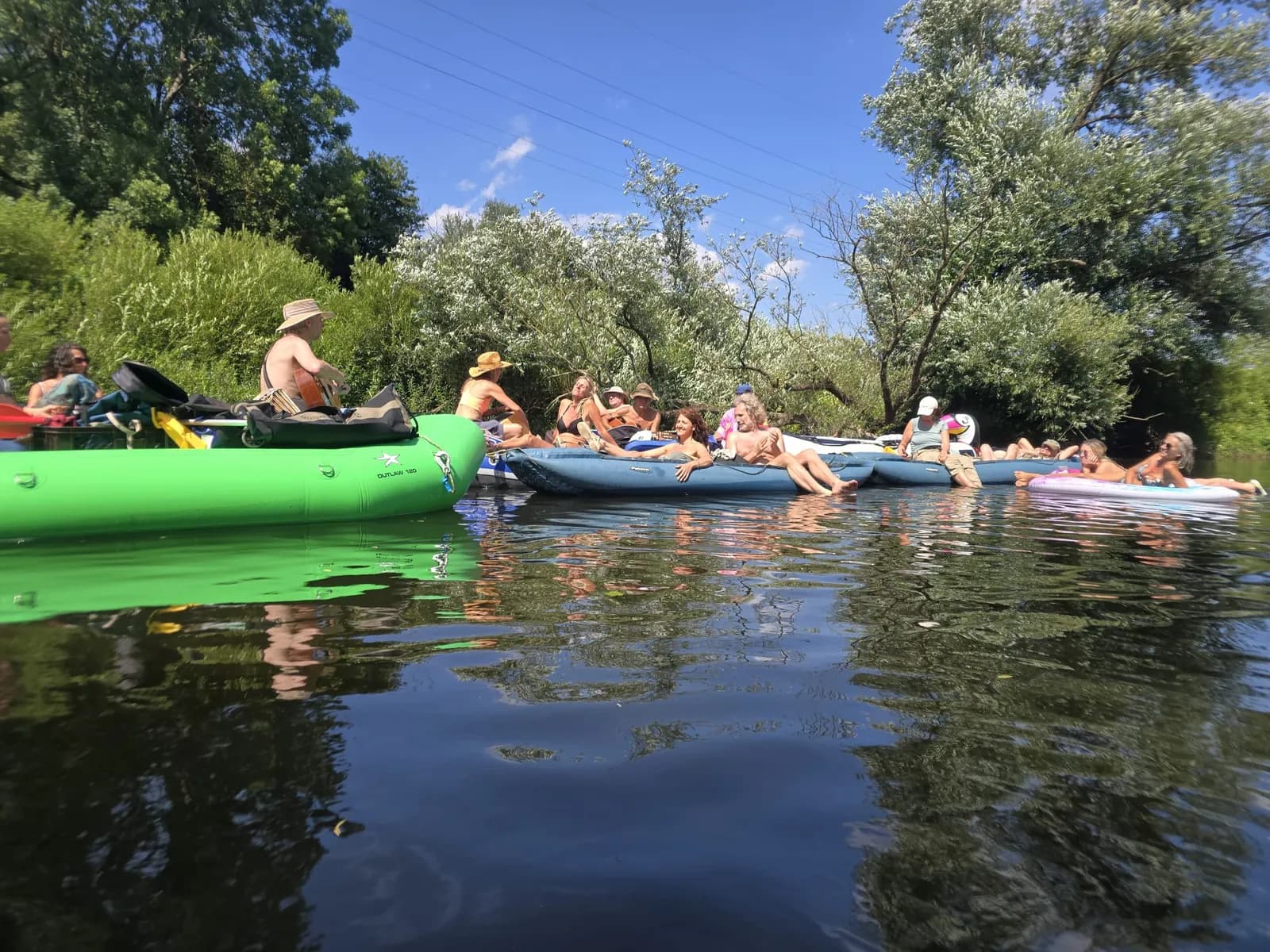 Eine Gruppe in Schlauchbooten auf der Mosel, links spielt ein Mann Gitarre